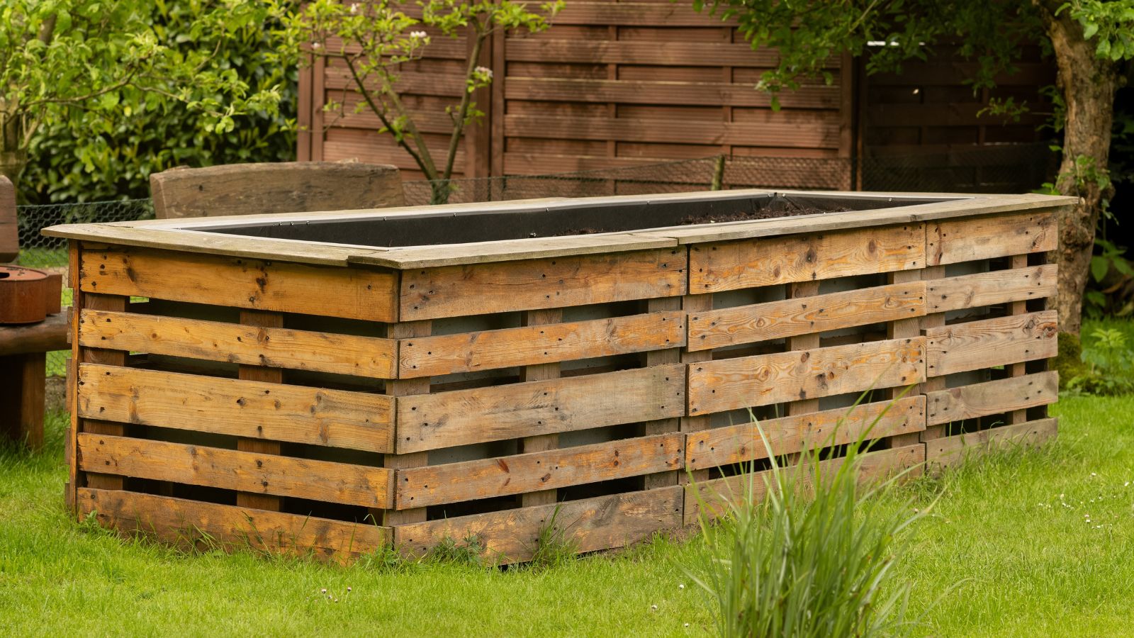 A shot of a wooden empty raised bed in a plot in a well lit backyard area