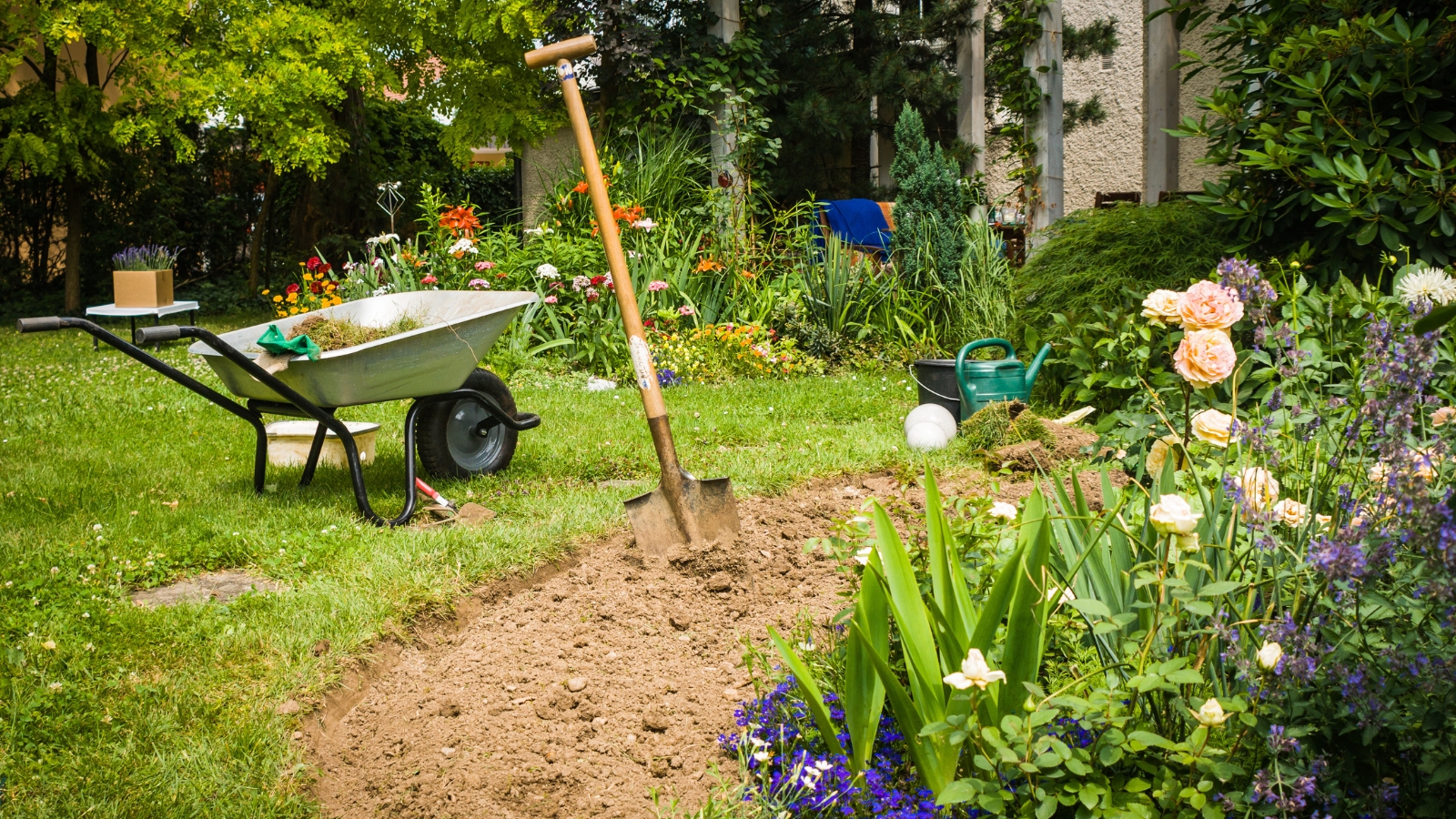 A person actively digging with a garden tool to create new beds, turning over a mound of dark earth, indicating preparation for planting.